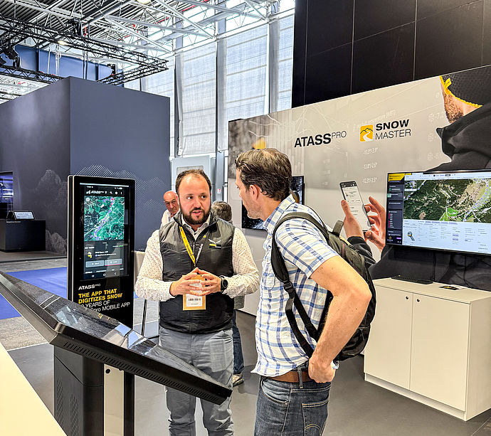 Mitarbeiter erklärt ATASSpro App am digitalen Display mit Snow Master Bildschirm im Hintergrund