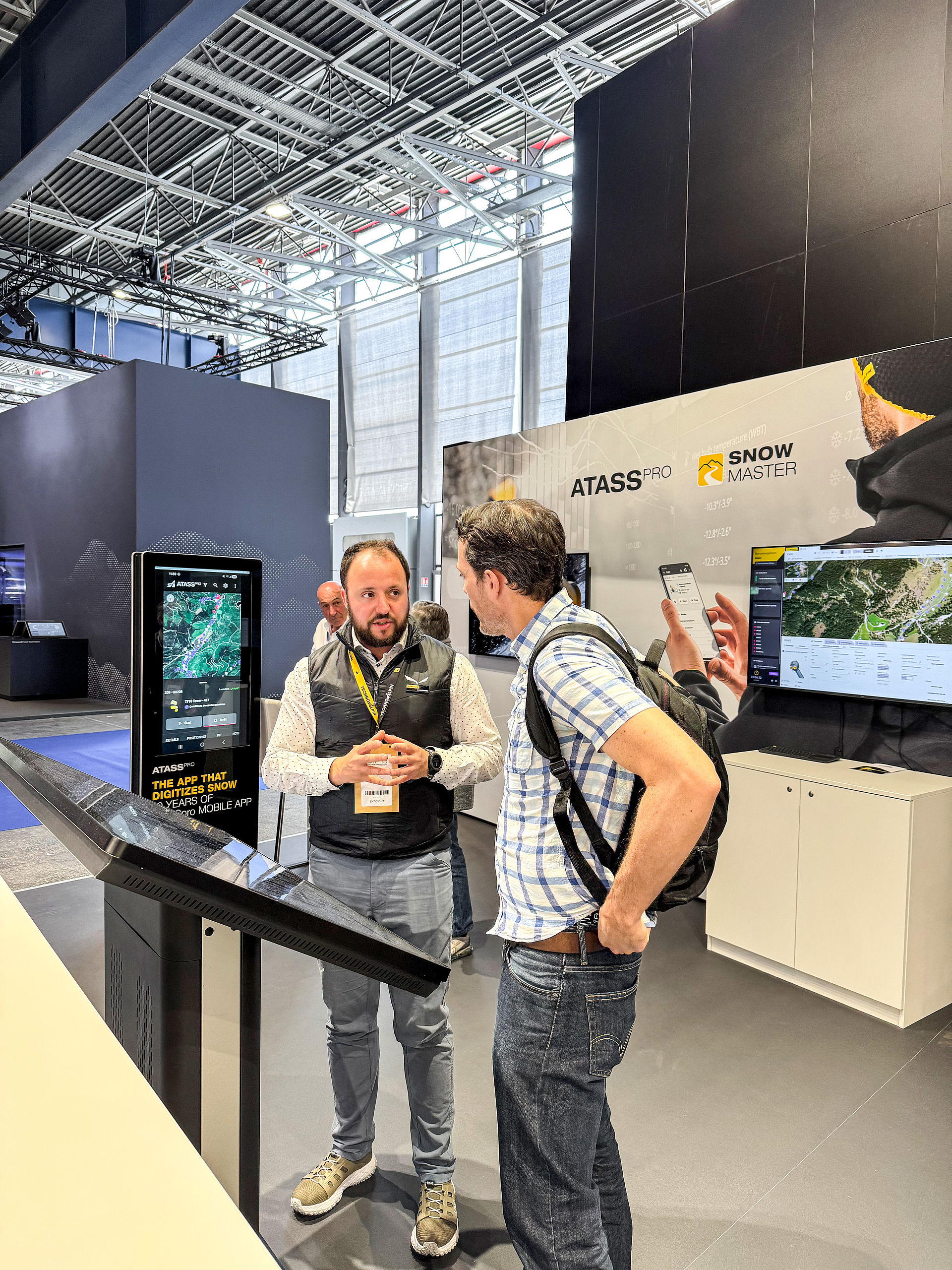 Mitarbeiter erklärt ATASSpro App am digitalen Display mit Snow Master Bildschirm im Hintergrund