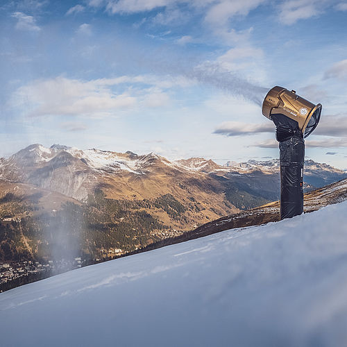 Goldene TechnoAlpin Schneekanone auf verschneitem Hang in Davos produziert Schnee mit Panoramablick ins Tal und auf die Alpen