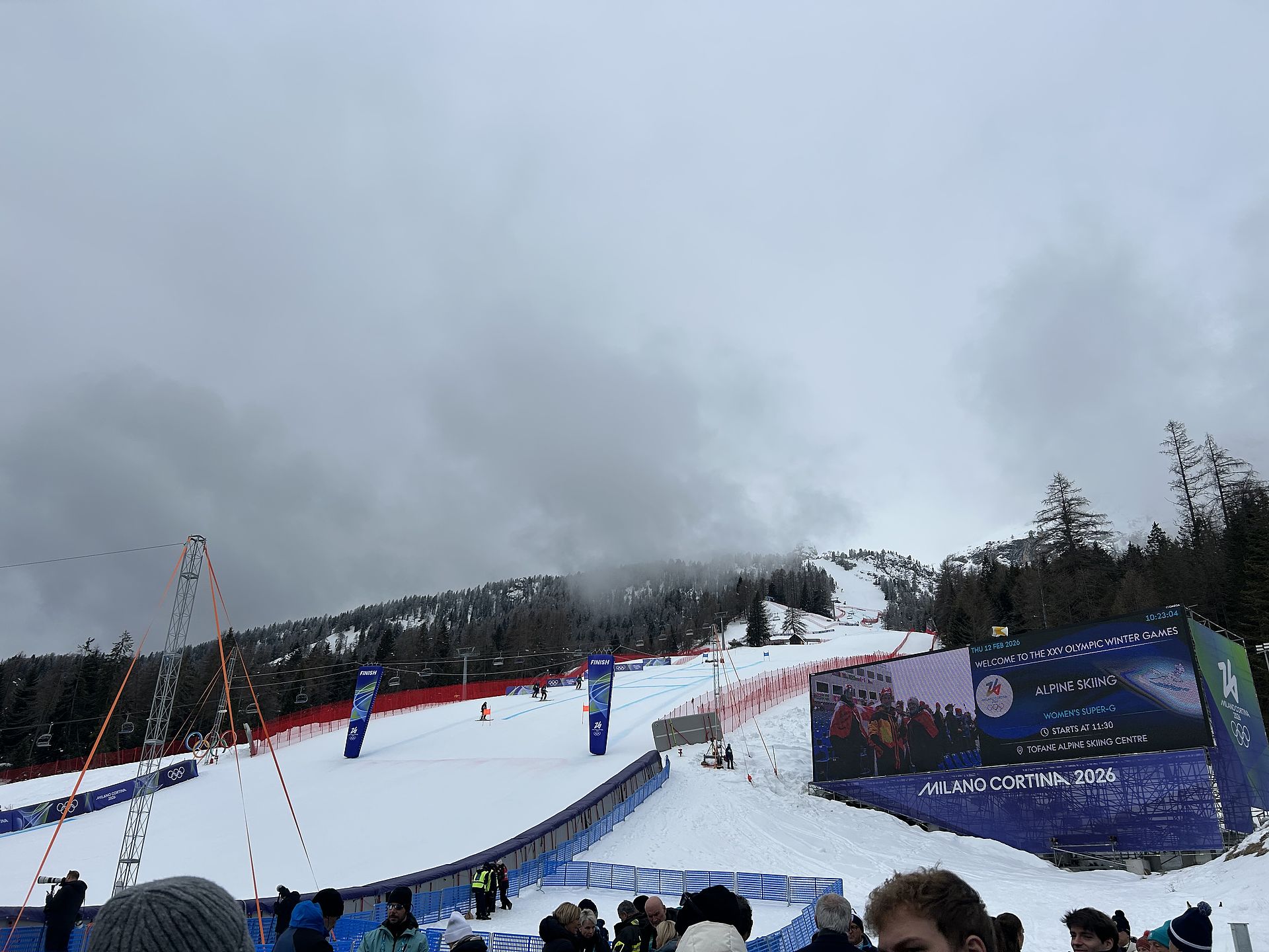 Bobsled track with Milano Cortina 2026 logo and church steeple in front of snowy mountain scenery