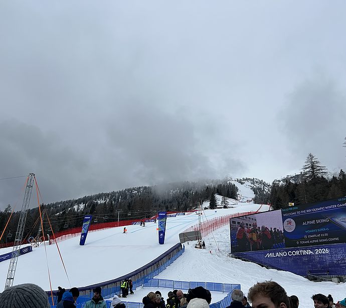 Bobsled track with Milano Cortina 2026 logo and church steeple in front of snowy mountain scenery