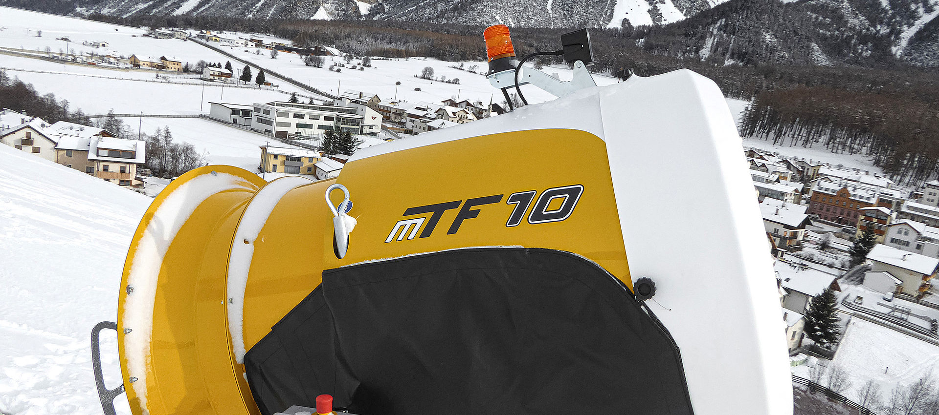 Enneigeur TechnoAlpin MTF 10 sur piste surplombant un village alpin enneigé