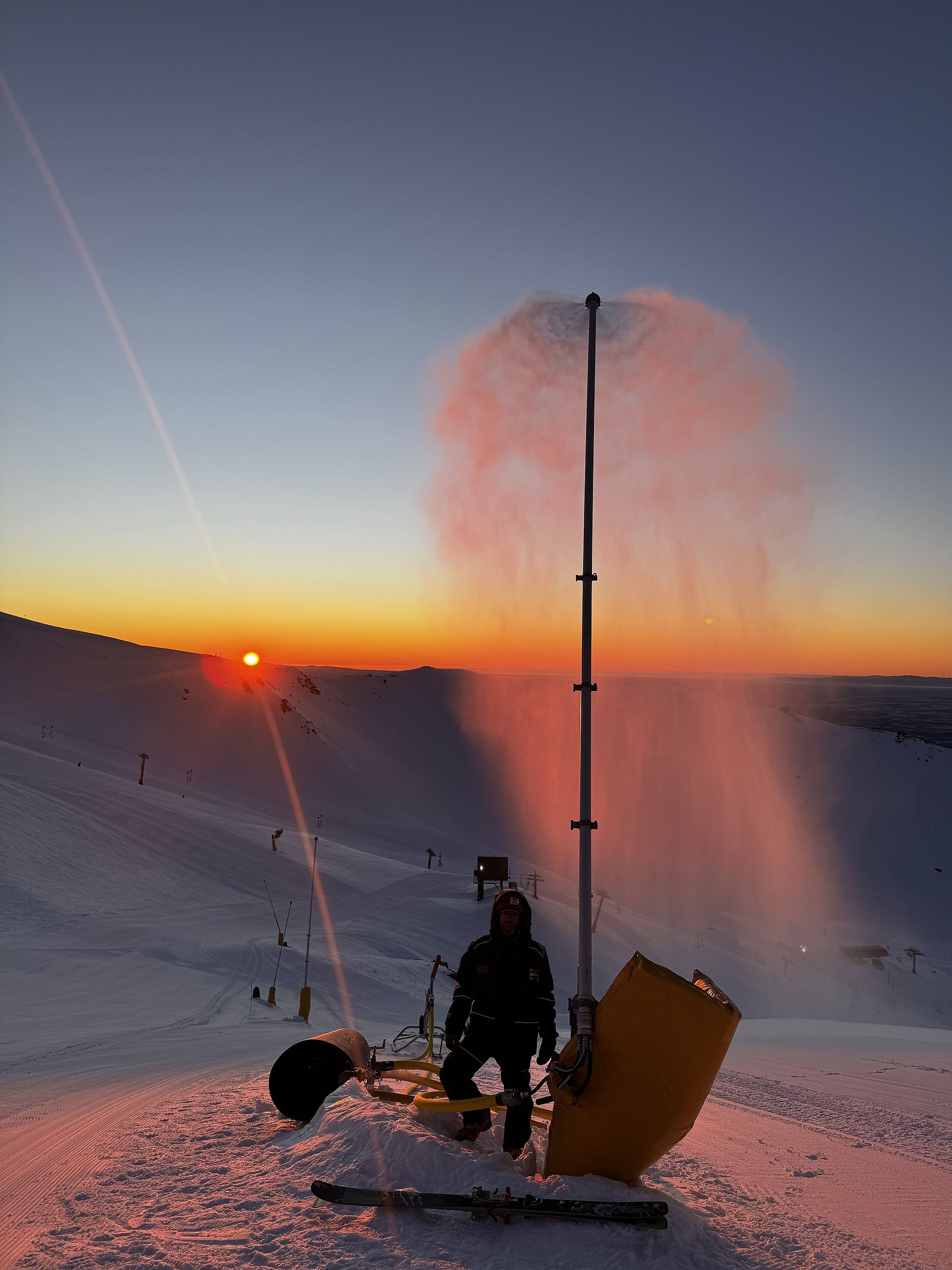 Schneilanze im Betrieb bei Sonnenuntergang mit Techniker auf verschneiter Piste
