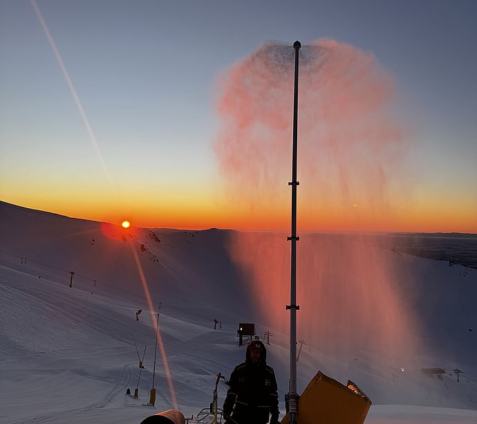 Schneilanze im Betrieb bei Sonnenuntergang mit Techniker auf verschneiter Piste