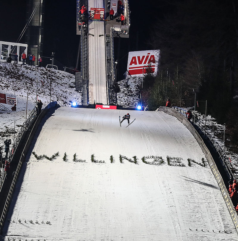 Skispringer im Flug über der beschneiten Schanze in Willingen bei Nacht