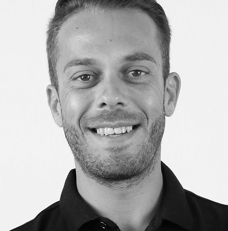 Daniel Koch, TechnoAlpin Mitarbeiter, Schwarz-Weiß-Portrait mit herzlichem Zahnlächeln, kurzem Haar und schwarzem Polo-Shirt