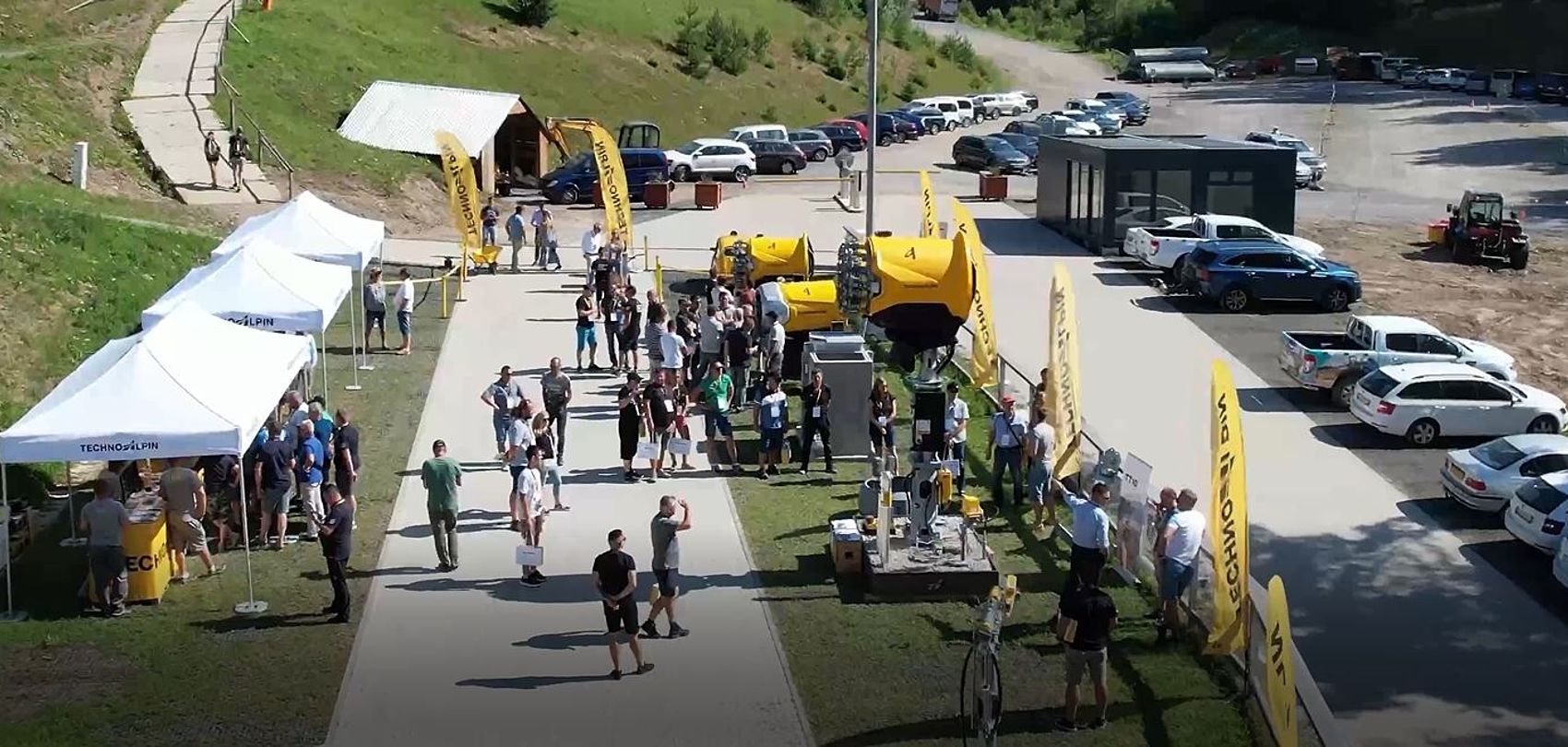 Aerial view of TechnoAlpin roadshow with yellow branded flags, white tents and snow guns on display
