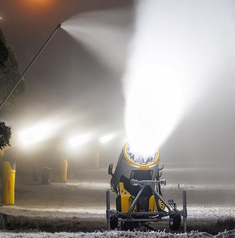 Gelbe TechnoAlpin Propellermaschine und Lanze produzieren bei Nacht unter Flutlicht Schnee