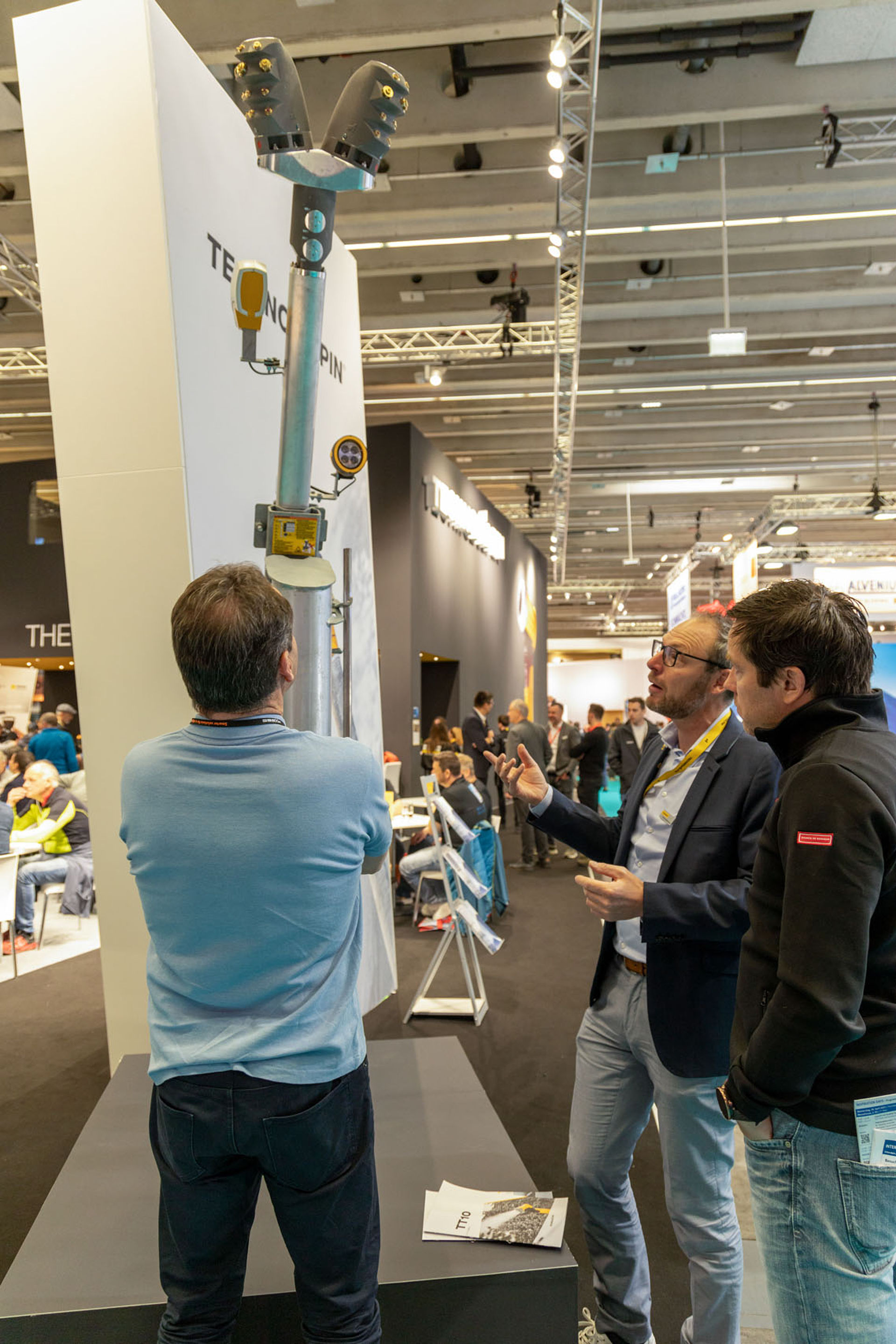 Zwei Männer in Businesskleidung diskutieren Schneelanze am TechnoAlpin Interalpin 2023 Stand, weiterer Besucher begutachtet das Gerät