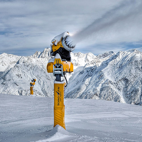 Gelbe TechnoAlpin Schneekanone in Aktion auf Skipiste mit Alpenpanorama
