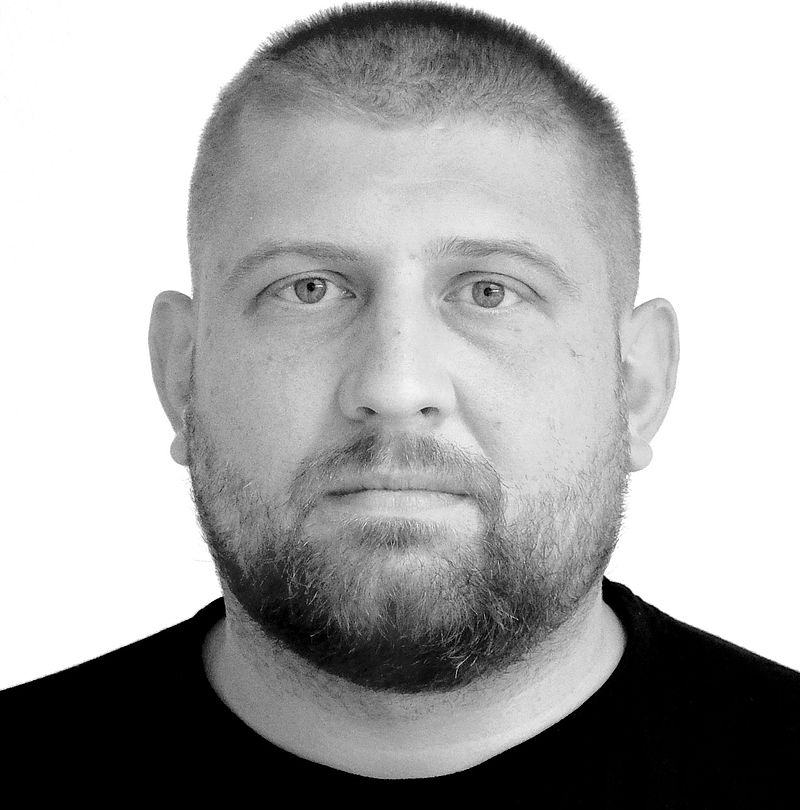 Tomasz Adamus, TechnoAlpin Mitarbeiter, Portrait mit sehr kurzem Haar, vollem Bart und neutralem Ausdruck in schwarzem T-Shirt