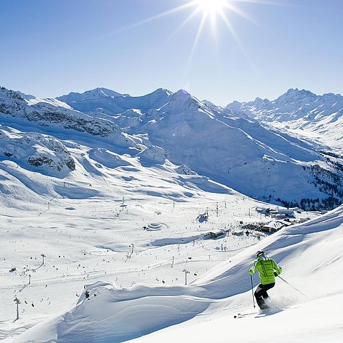 Skiläufer auf sonnenbeschienener Piste in der Silvretta Arena mit Blick auf Alpengipfel und Liftanlagen