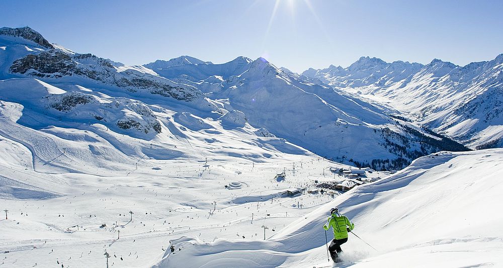 Skiläufer auf sonnenbeschienener Piste in der Silvretta Arena mit Blick auf Alpengipfel und Liftanlagen