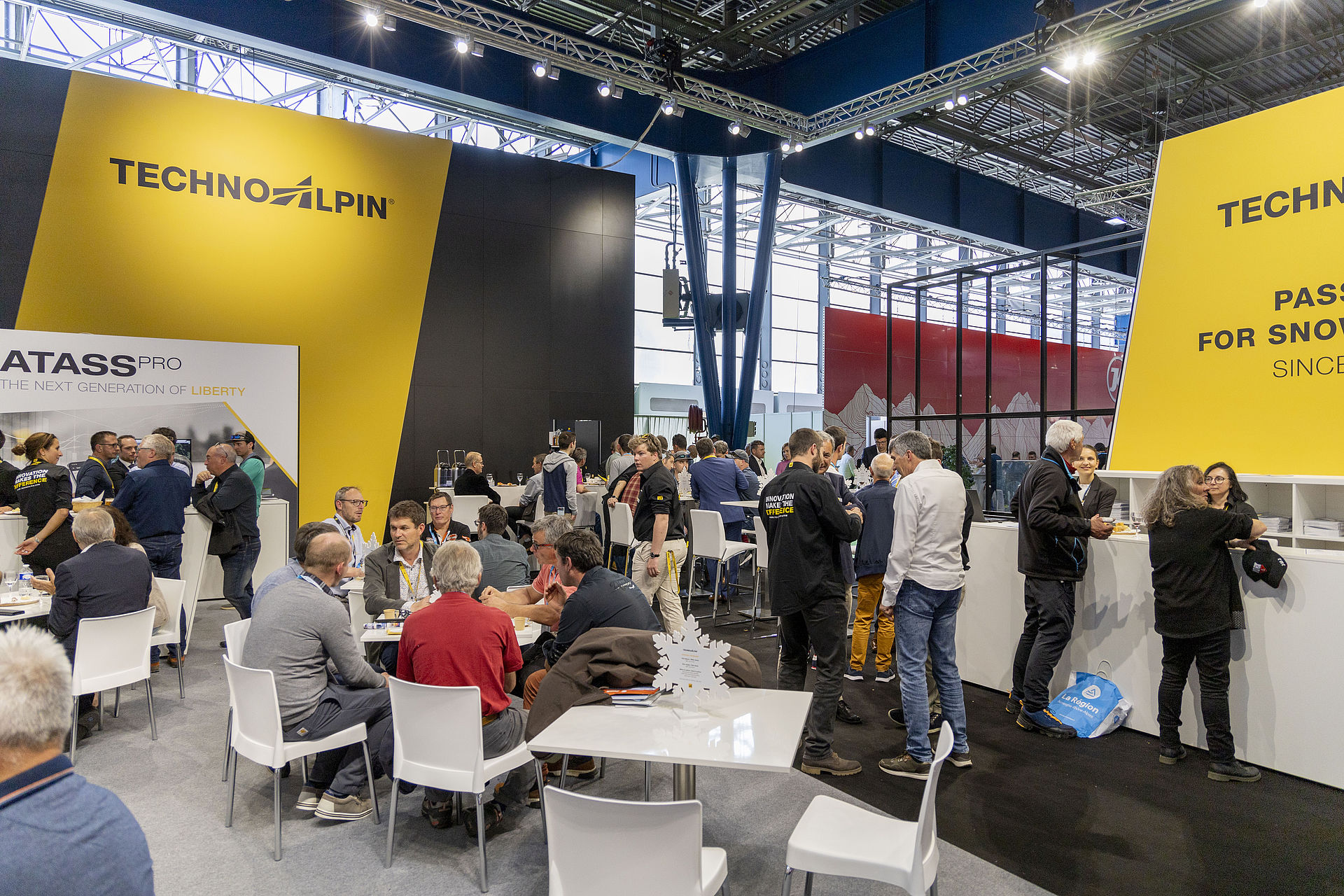 Busy TechnoAlpin trade show stand with yellow-black branding and networking area.