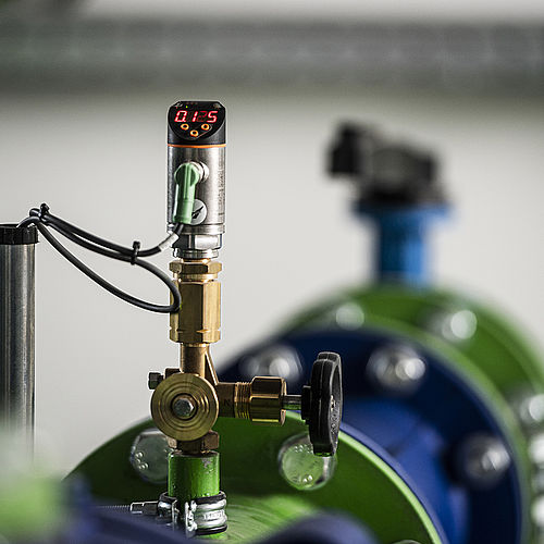Pumpstation Innenansicht mit großer blauer Vertikalpumpe, grünen Rohrleitungen und Steuerungsmonitor
