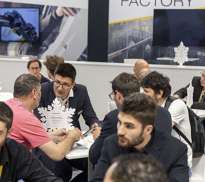 Visitors and employees talking at high tables in Snow Factory area of trade show stand.