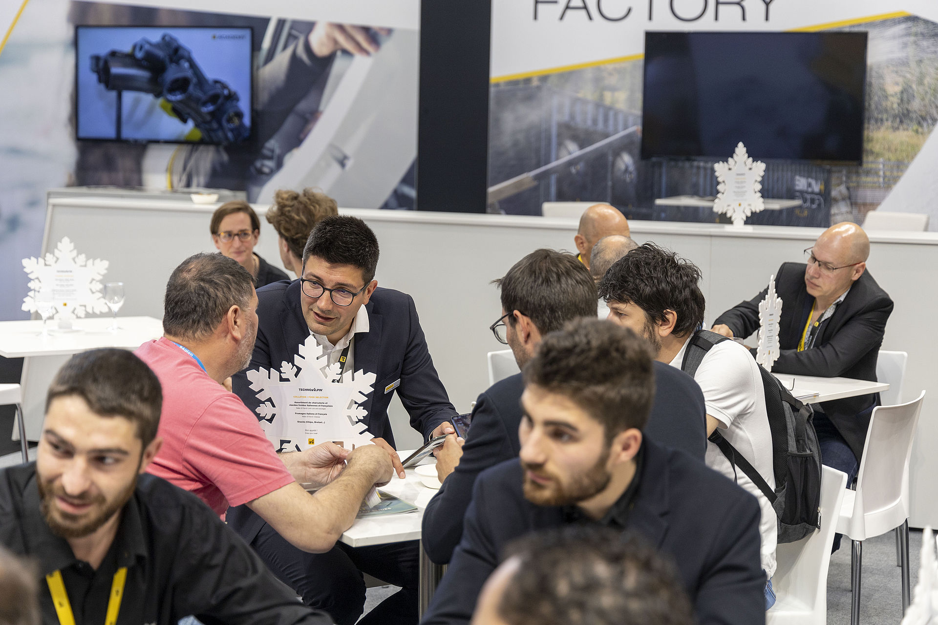 Visitors and employees talking at high tables in Snow Factory area of trade show stand.