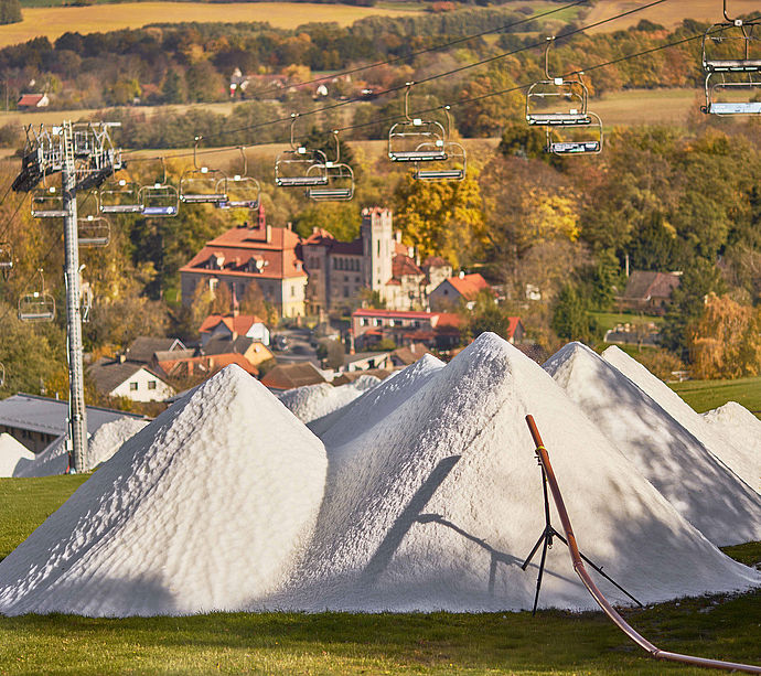 Schneehaufen der SnowFactory auf grüner Wiese mit Sessellift und herbstlicher Landschaft