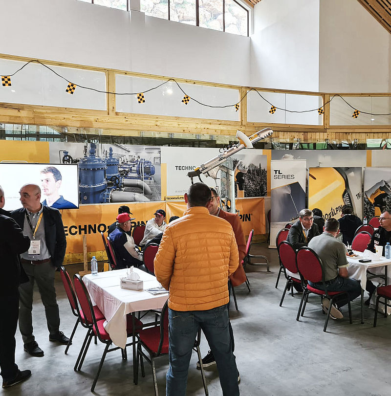 Sala eventi TechnoAlpin con tavoli alti, ospiti e lancia da neve esposta.