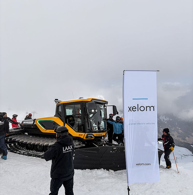 Dameuse électrique orange Xelom avec bannière dans la neige lors d'une présentation