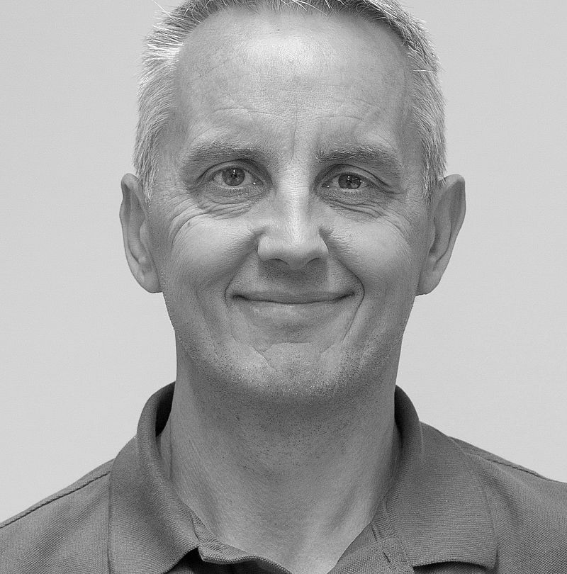 Alain De Cian, TechnoAlpin Mitarbeiter, Schwarz-Weiß-Portrait mit grauem Kurzhaar und freundlichem Lächeln in dunklem Kappa-Polo-Shirt