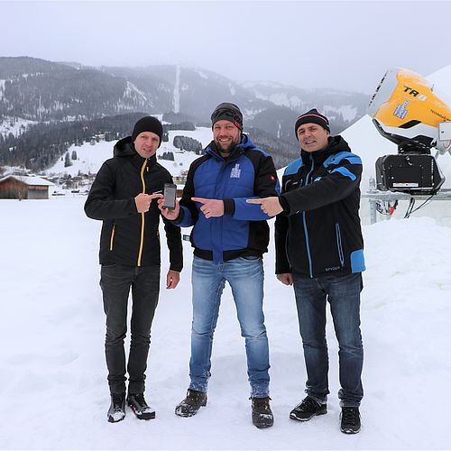 Drei Männer in der Tiroler Zugspitz Arena mit TechnoAlpin App auf Smartphone und TR8 Schneekanone