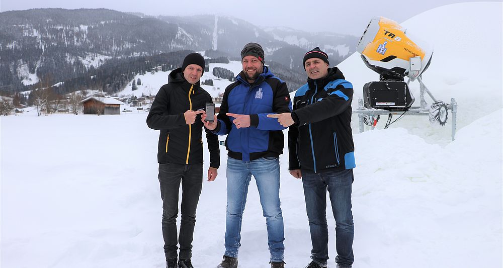 Drei Männer in der Tiroler Zugspitz Arena mit TechnoAlpin App auf Smartphone und TR8 Schneekanone