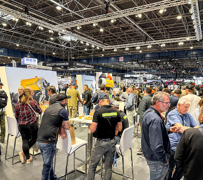 Belebter TechnoAlpin-Messestand mit Besuchern an Stehtischen in großer Messehalle
