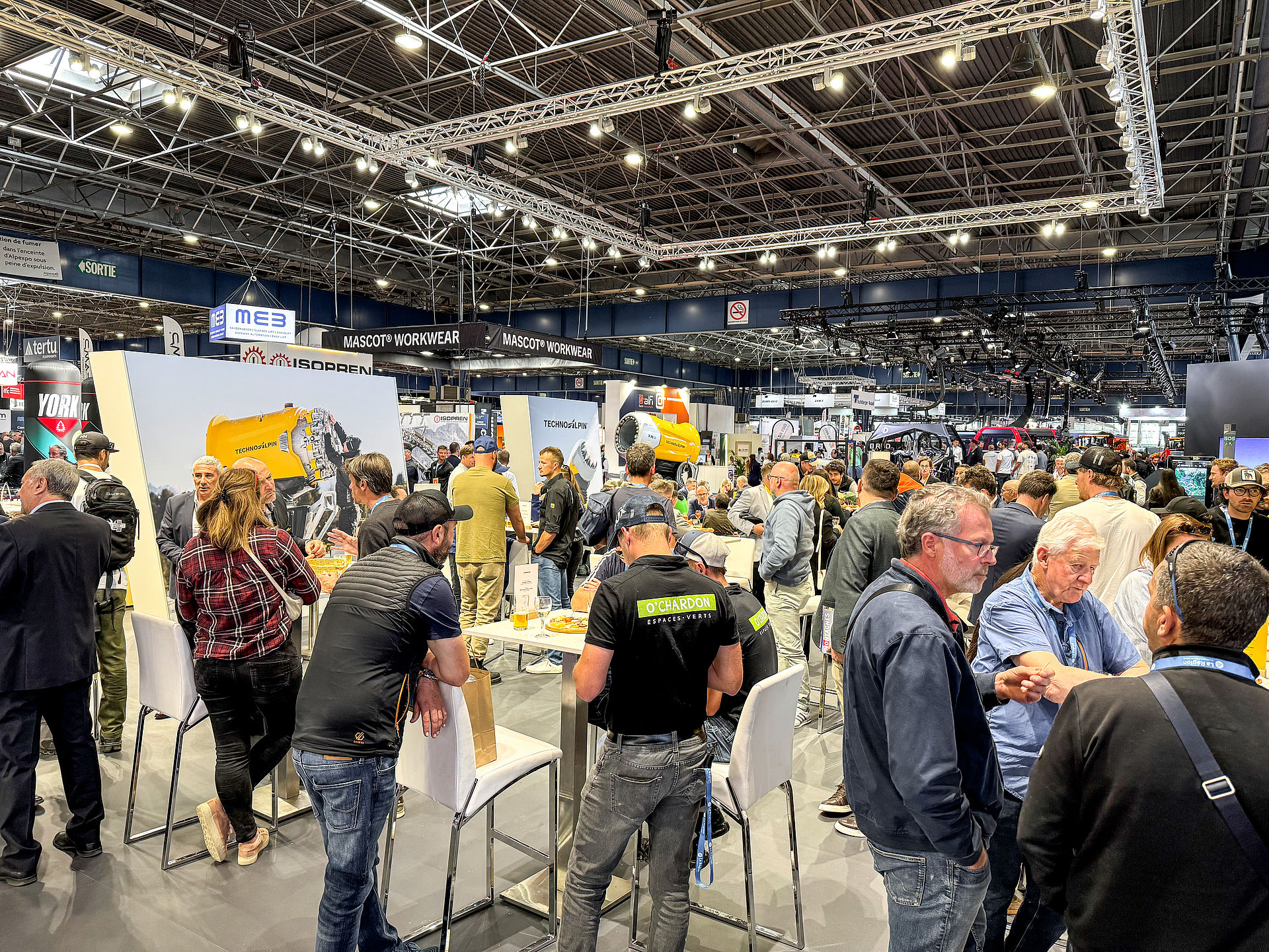 Belebter TechnoAlpin-Messestand mit Besuchern an Stehtischen in großer Messehalle