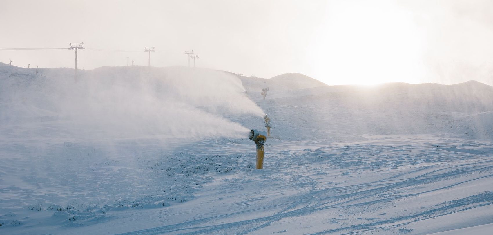 Schneelanze sprüht Schnee auf Piste bei Gegenlicht im Skigebiet Coronet Peak