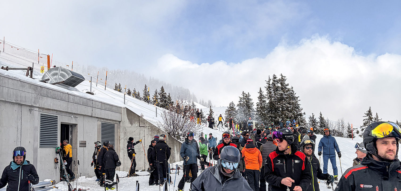 Groupe de skieurs se rassemble sur piste devant gare amont lors d'événement dans le domaine skiable