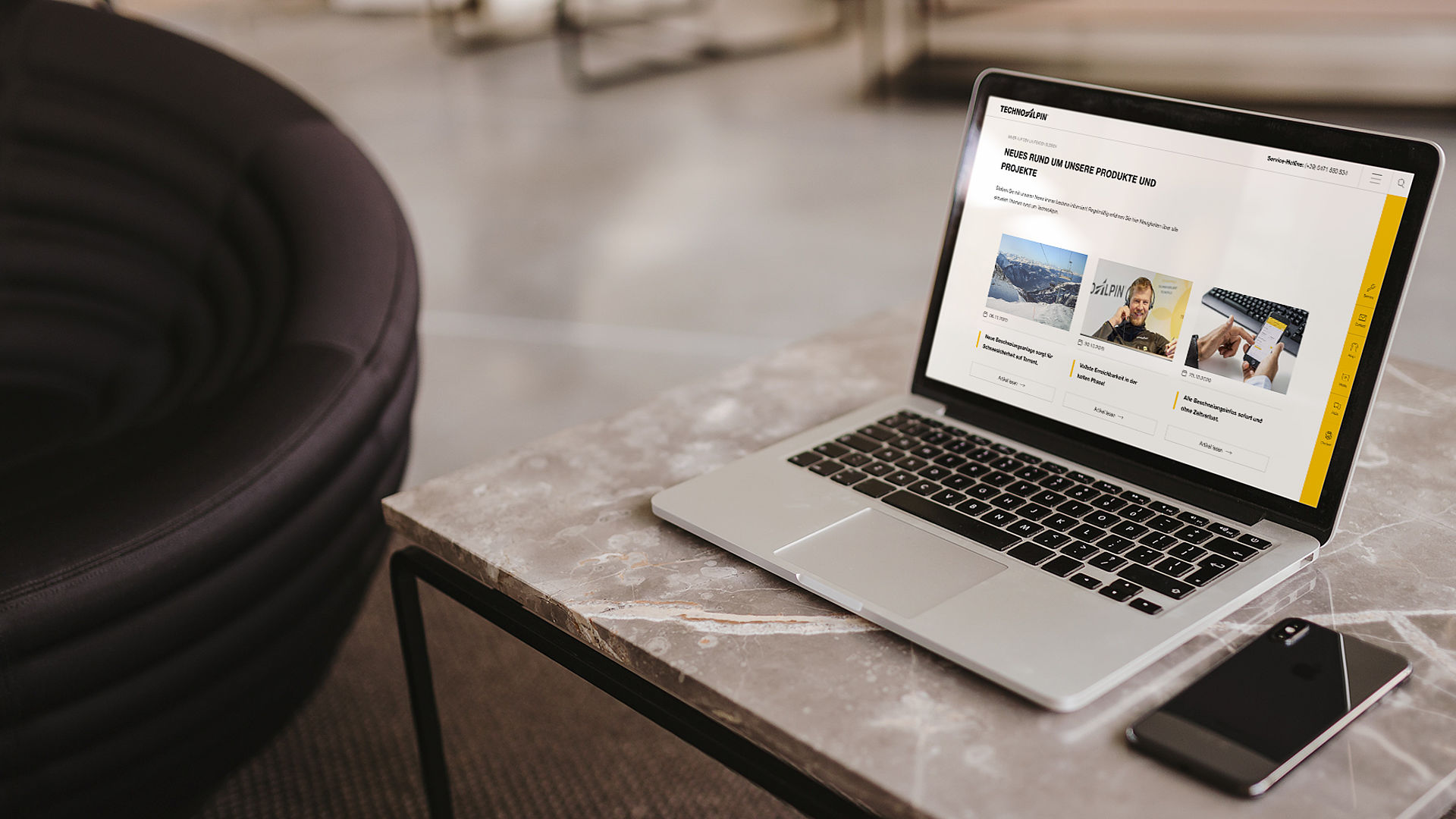 Laptop zeigt TechnoAlpin News-Portal mit Produktinformationen auf Marmortisch im Loungebereich