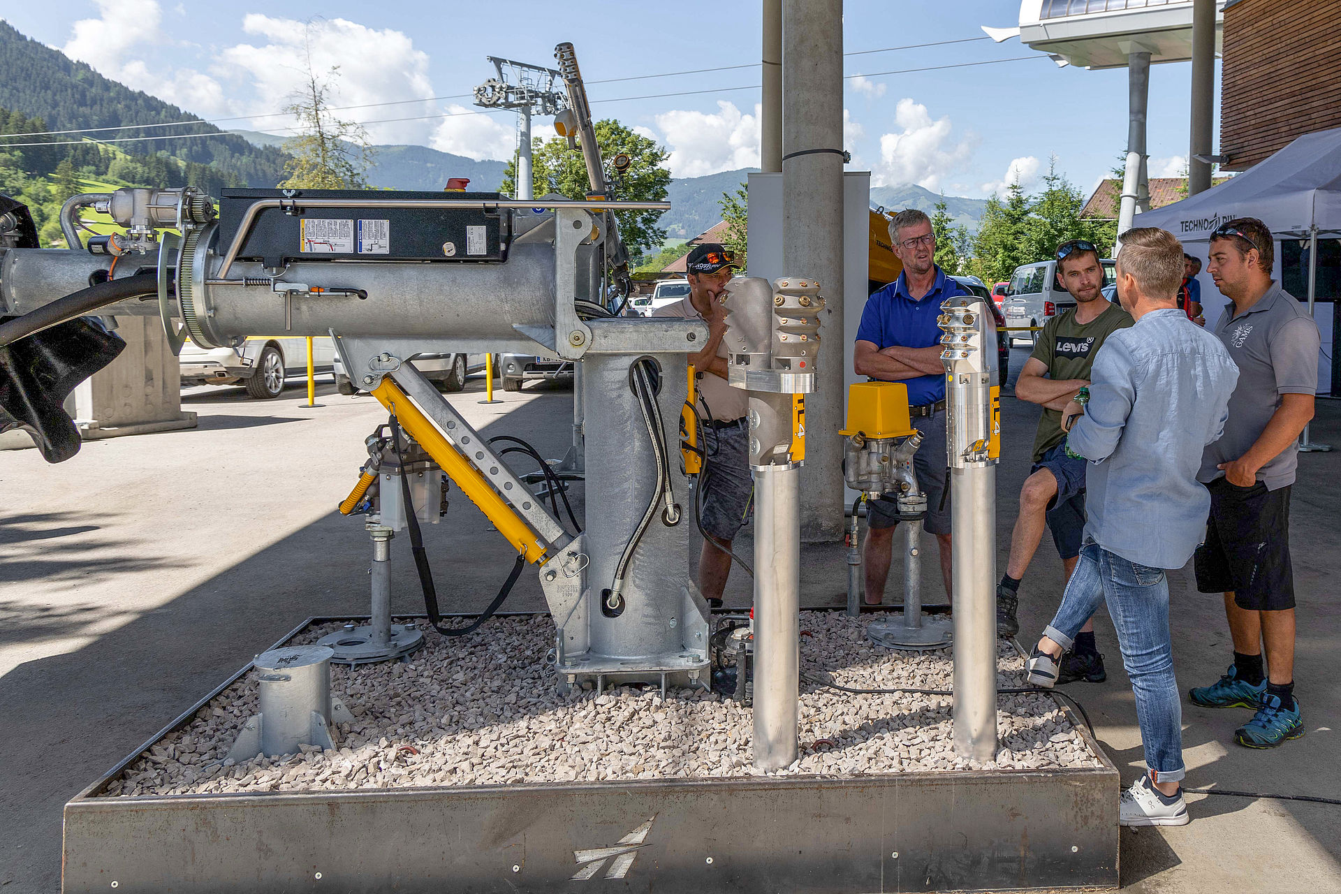 Participants examining snow lance and tapping stations at exhibition area with mountain panorama.
