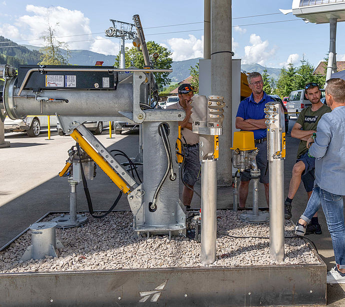 Participants examining snow lance and tapping stations at exhibition area with mountain panorama.