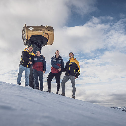 Vier Männer mit goldenem TechnoAlpin TT10 Nr. 1000 auf Davoser Bergrücken mit dramatischem Alpenpanorama