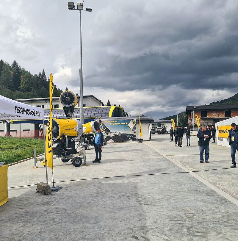TechnoAlpin outdoor demo with white tents and mobile yellow fan snow gun near gondola station