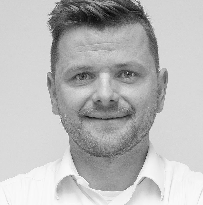 Benjamin Poetz, TechnoAlpin Mitarbeiter, Schwarz-Weiß-Portrait mit warmem Lächeln und kurzem blondem Haar vor hellem Studiohintergrund