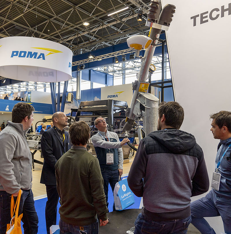 Visitor group listening to snow lance product presentation at TechnoAlpin trade show stand.
