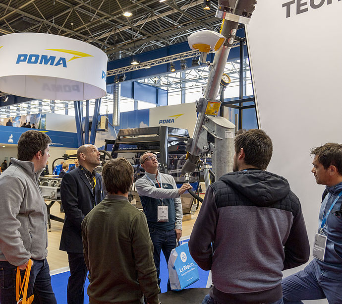 Visitor group listening to snow lance product presentation at TechnoAlpin trade show stand.