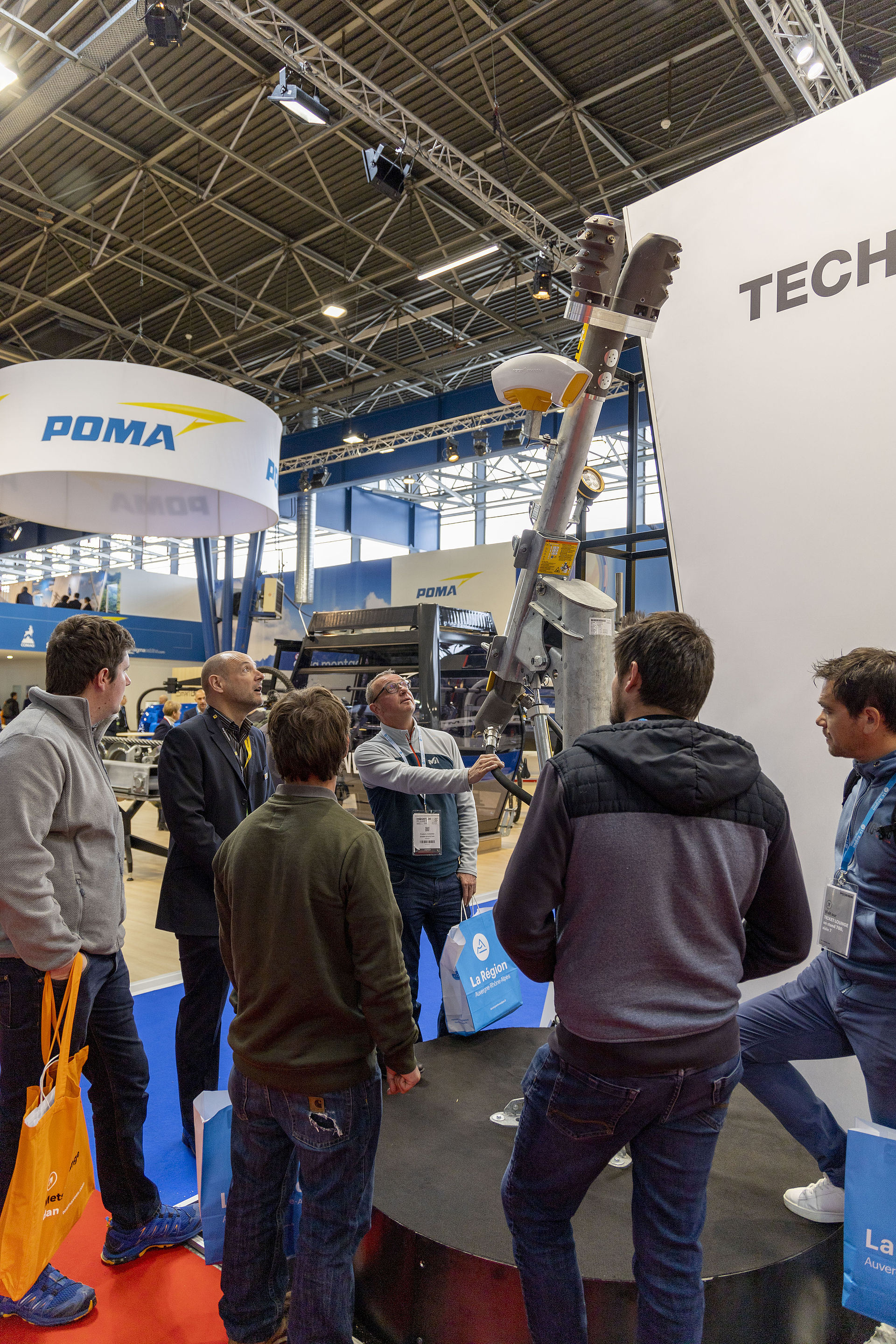 Visitor group listening to snow lance product presentation at TechnoAlpin trade show stand.