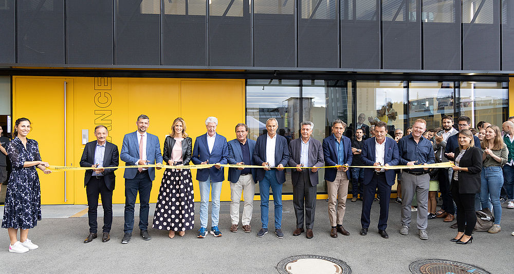 Cerimonia di inaugurazione TechnoAlpin: gruppo in abiti formali taglia insieme un nastro giallo TechnoAlpin davanti a moderno edificio aziendale