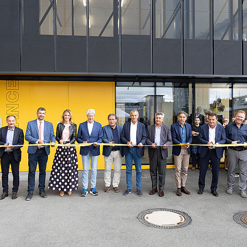 Cerimonia di inaugurazione TechnoAlpin: gruppo in abiti formali taglia insieme un nastro giallo TechnoAlpin davanti a moderno edificio aziendale