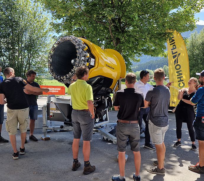 Group of ski resort employees at product presentation of yellow TechnoAlpin propeller snow gun.