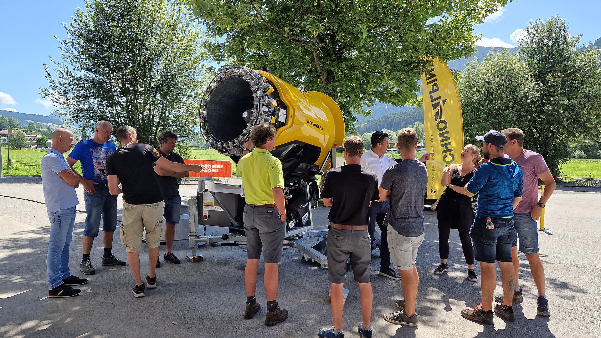 Group of ski resort employees at product presentation of yellow TechnoAlpin propeller snow gun.