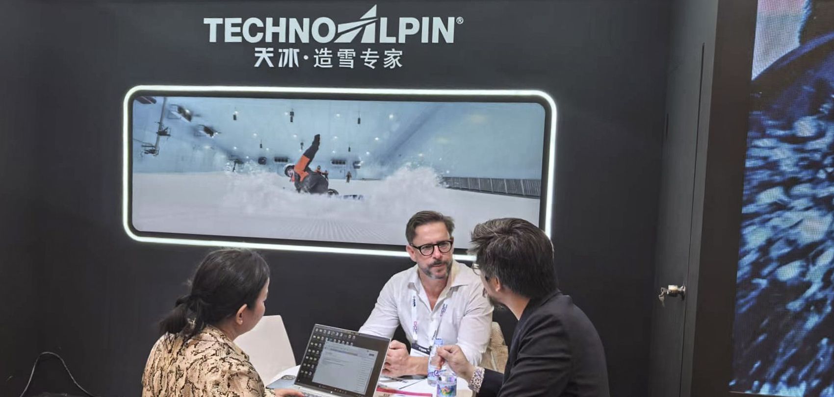 TechnoAlpin trade fair booth in China with business conversation in front of screen