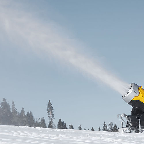 Gelber TechnoAlpin TR10 Schneeerzeuger im Einsatz auf verschneiter Piste mit Schneestrahl.