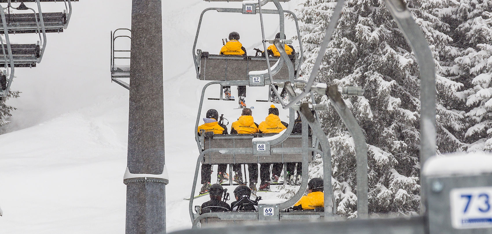 TechnoAlpin Mitarbeiter in gelben Jacken auf Sesselliftfahrt bei dichtem Schneefall im Skigebiet