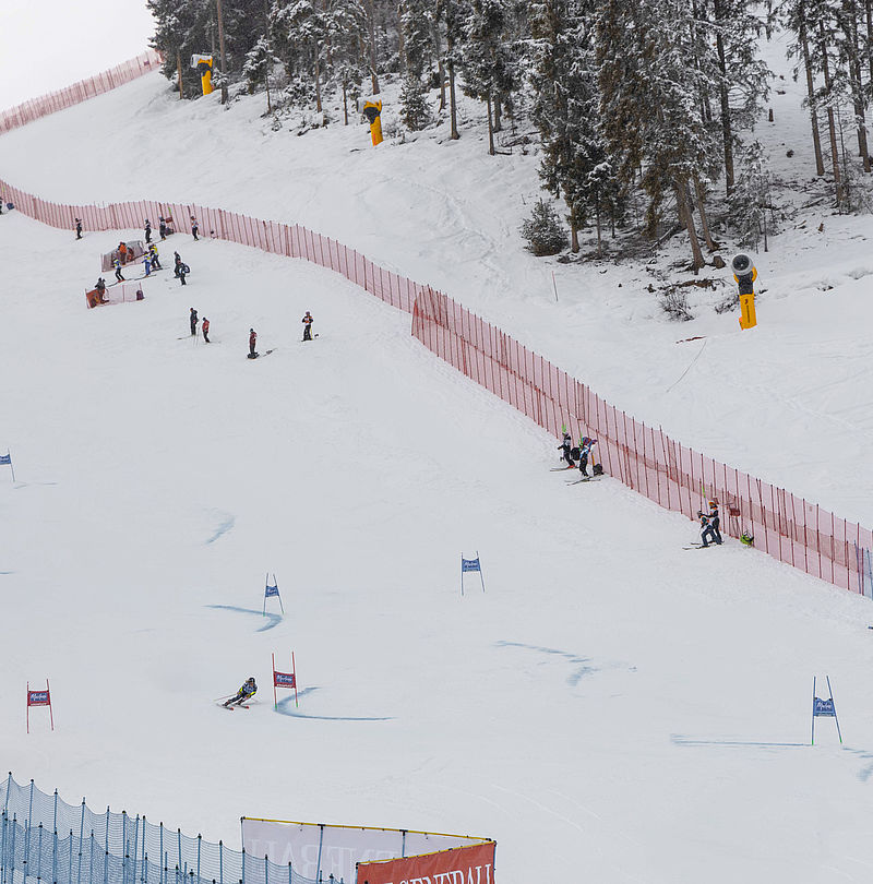 Skirennläufer auf Slalompiste mit roten Sicherheitsnetzen, Schneekanonen am Pistenrand und Generali-Werbebande im Zielbereich