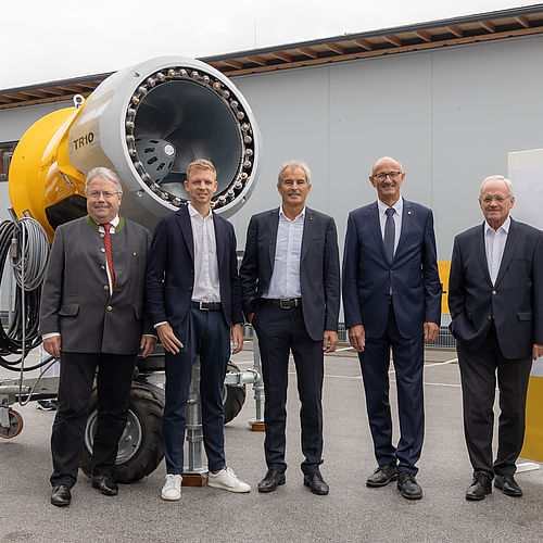 Fünf Männer beim 25-Jahre-Jubiläum von TechnoAlpin Österreich (TAAT) mit gelbem TR10 Schneeerzeuger