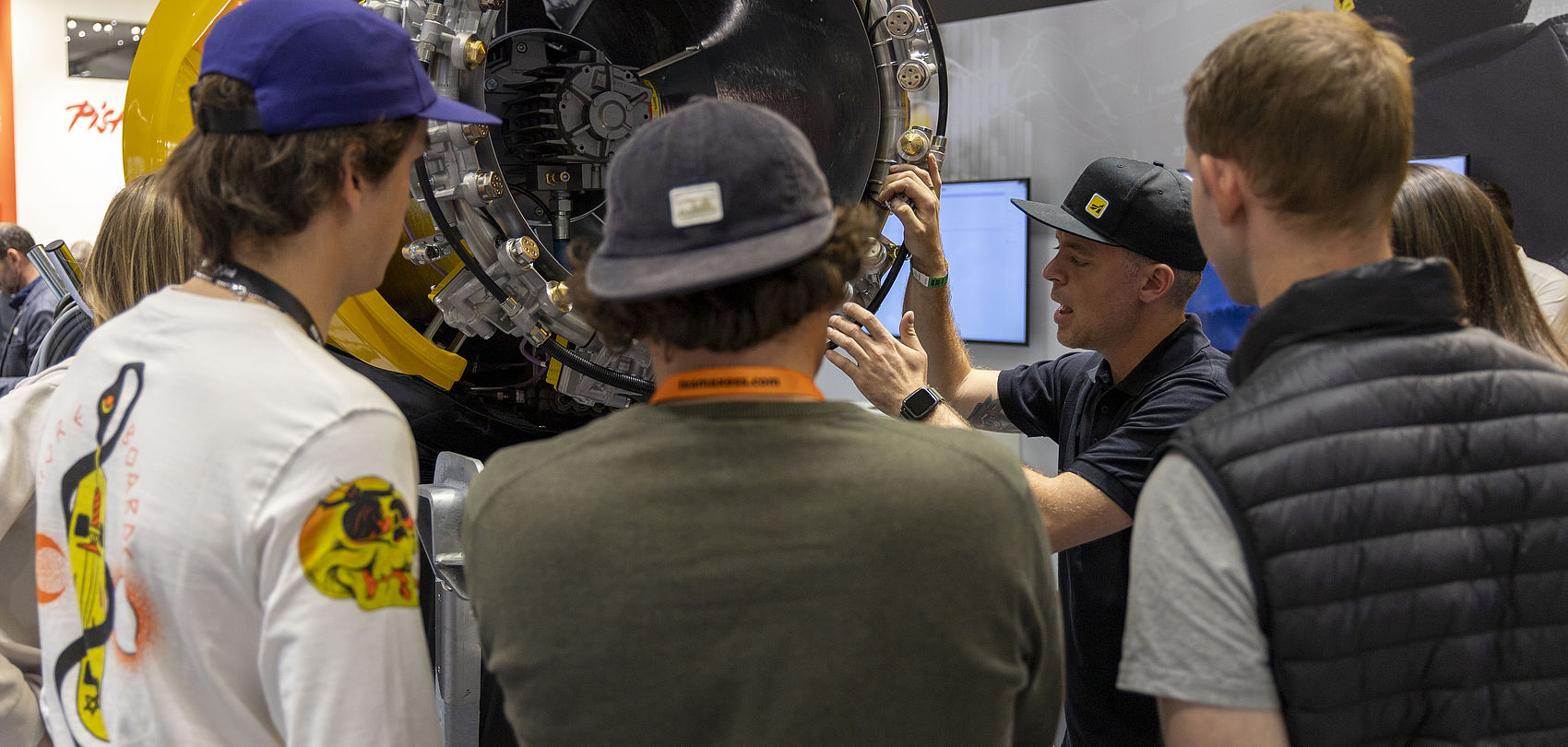 Group of young visitors looking at interior of yellow snow gun, technician explains the mechanics